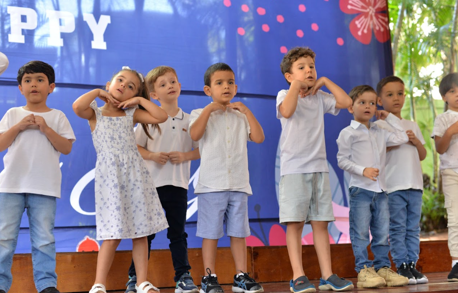 Alunos da Casa de Vo fazendo gesto de coracao no palco durante apresentacao de Dia das Maes